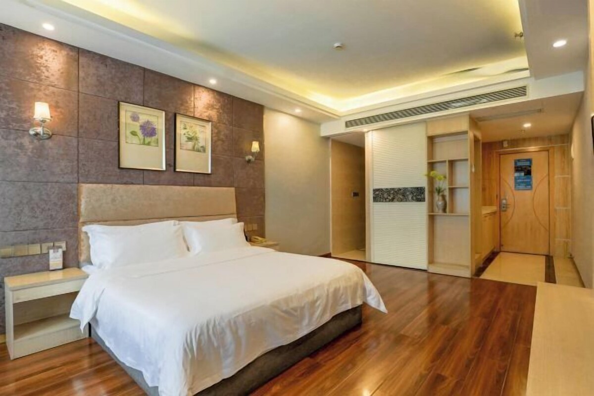 A hotel room with a large bed, bedside tables, a wardrobe, and a bathroom with a shower and toilet.
