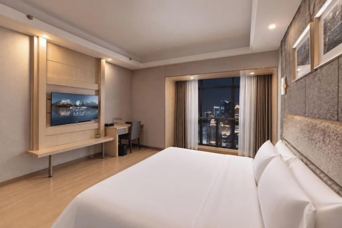 A hotel room with a bed, a desk, a TV, and a city view.