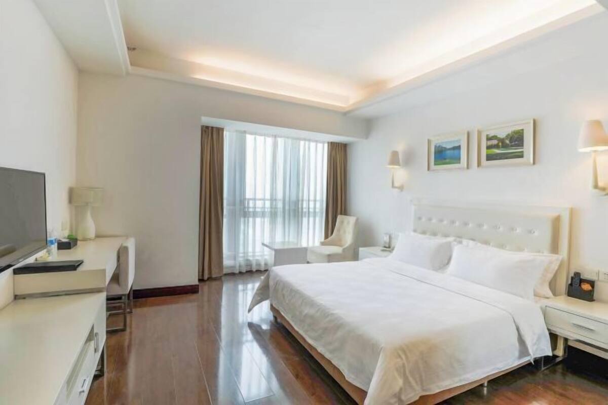 A hotel room with a large bed, a desk, a chair, a TV, and a window with curtains.