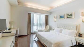 A hotel room with a large bed, a desk, a chair, a TV, and a window with curtains.