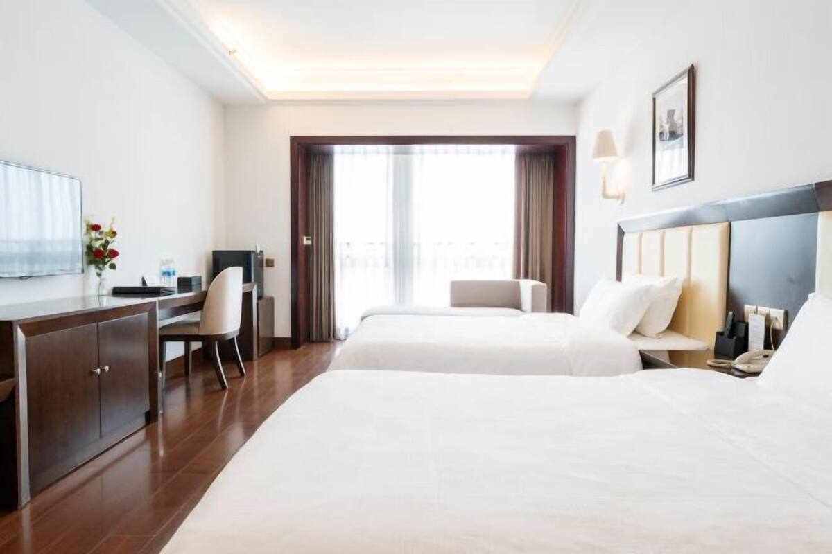 A hotel room with a bed, a desk, a chair, a TV, and a window with curtains.