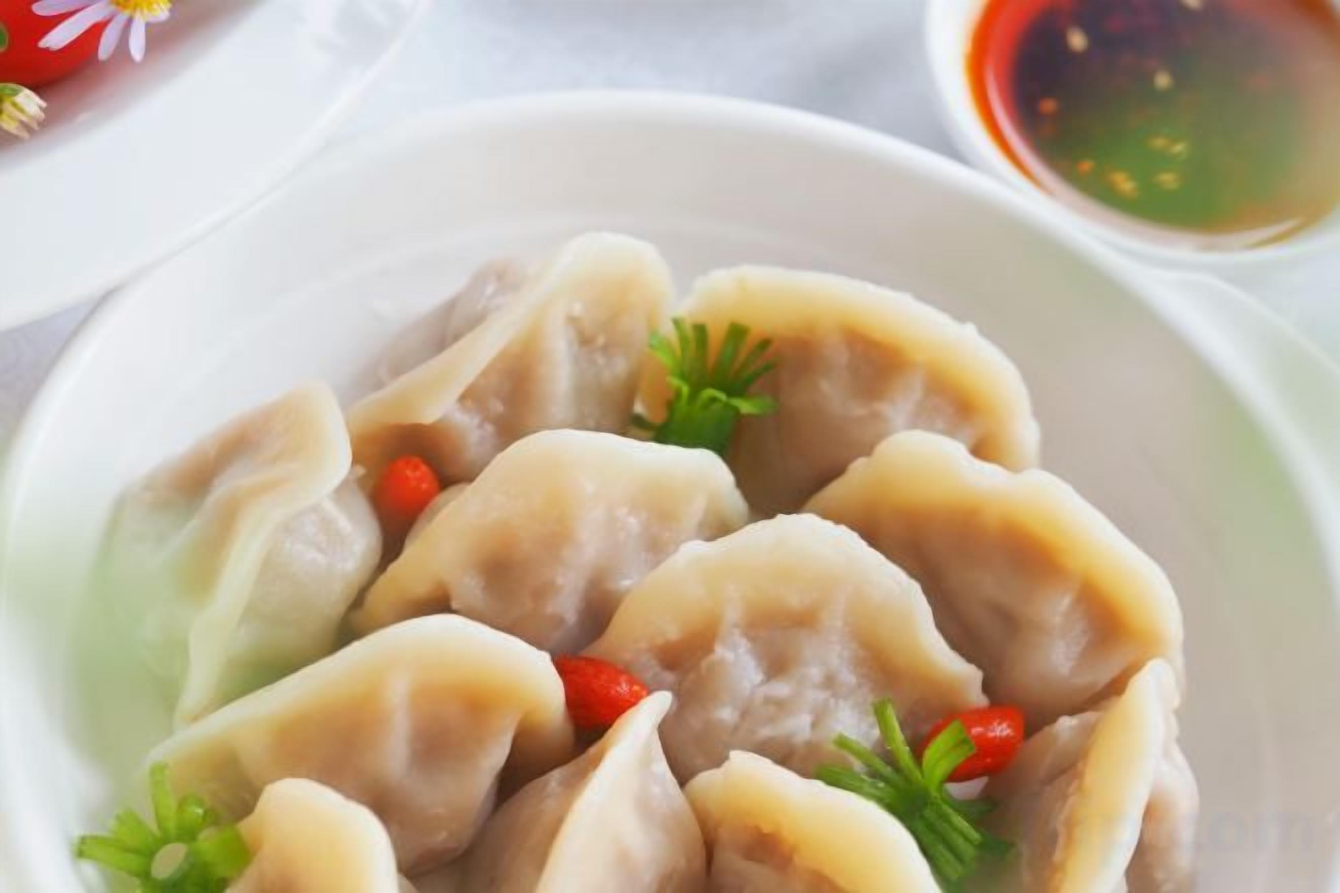 A plate of dumplings garnished with red chili and parsley, accompanied by a small bowl of dipping sauce.