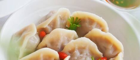 A plate of dumplings garnished with red chili and parsley, accompanied by a small bowl of dipping sauce.
