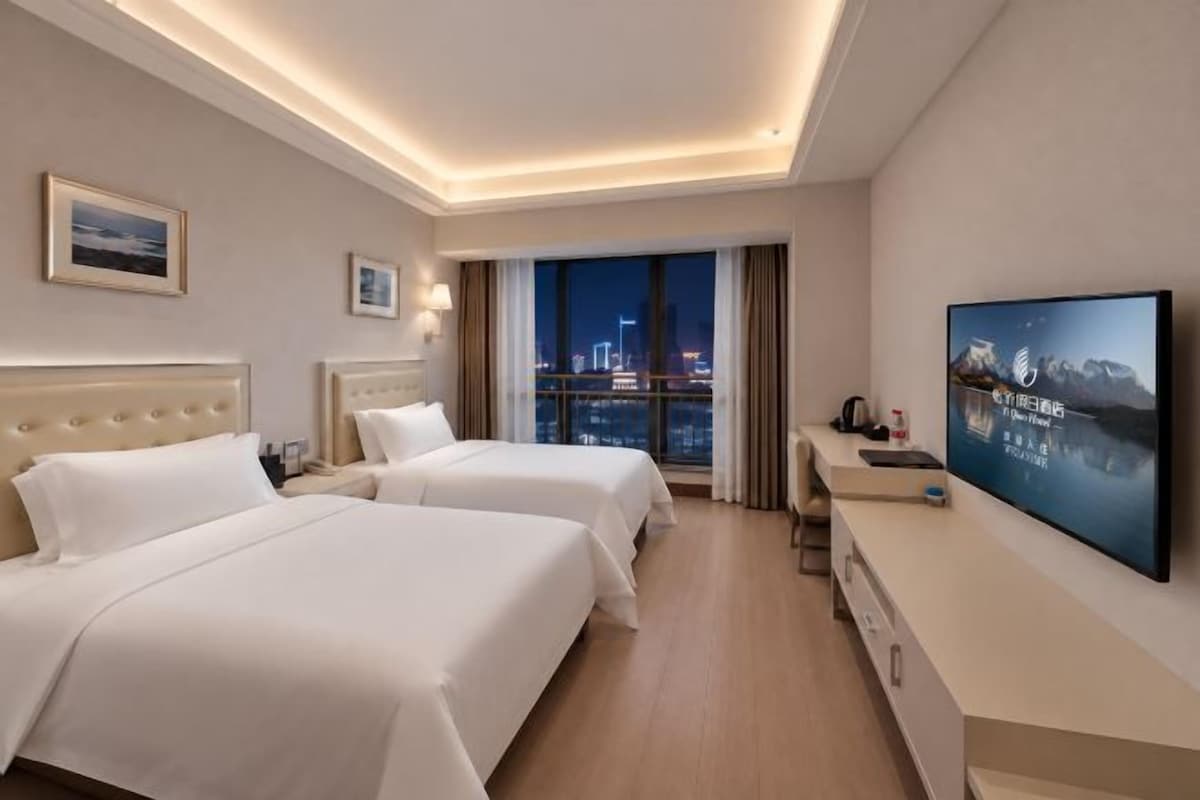 A hotel room with two beds, a TV, a desk, and a view of the city at night.