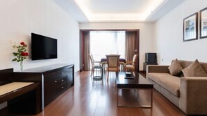 A modern hotel room with a flat-screen TV, a sofa, a dining table with chairs, and a small TV on a side table. - Yi Qiao Hotel (Chengdu)