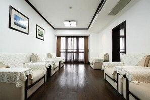 Habitación de hotel con un largo pasillo, varias camas y un amplio ventanal con cortinas.