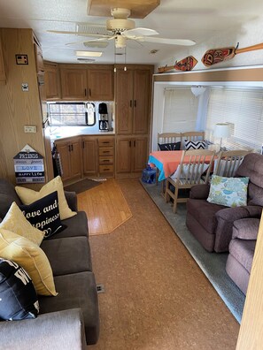 Interior compacto de una caravana con kitchenette, comedor y zona de estar con sofá y sillones.