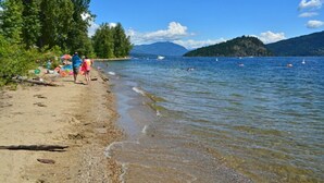 Una playa con agua cristalina, una orilla arenosa y una colina boscosa al fondo.