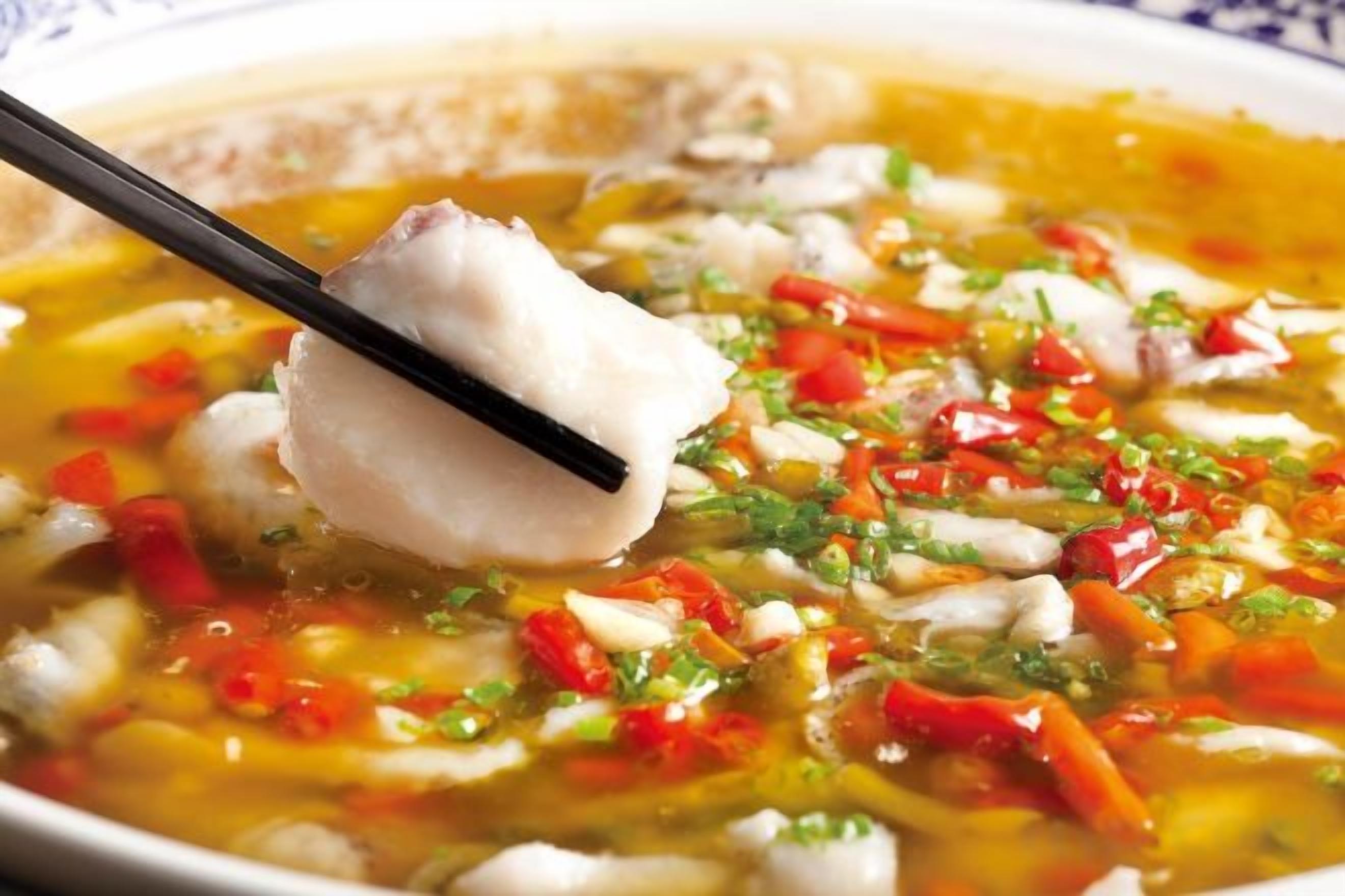 Un tazón de sopa con un trozo de pescado y verduras picadas.
