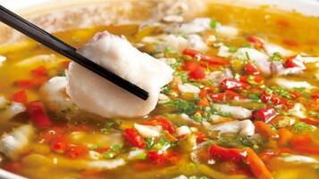 Un tazón de sopa con un trozo de pescado y verduras picadas.
