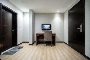 A room with a desk, chair, TV, and two doors. - Teng Chuan Hotel (Lichuan)
