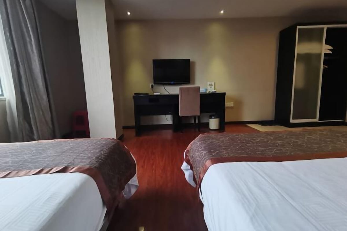 A hotel room with two beds, a desk with a TV, and a wardrobe.
