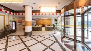 A hotel lobby with a reception desk, a check-in counter, a large pillar, a potted plant, and a glass entrance. - Teng Chuan Hotel (Lichuan)