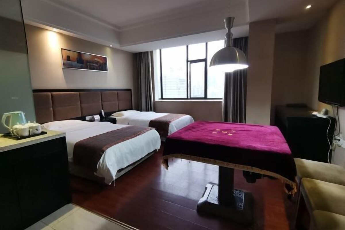 A hotel room with two beds, a desk with a lamp, a TV, and a window with curtains.