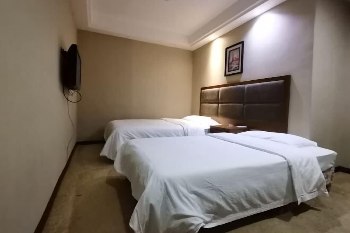 A hotel room with two beds, a headboard, a wall-mounted TV, and a framed picture.