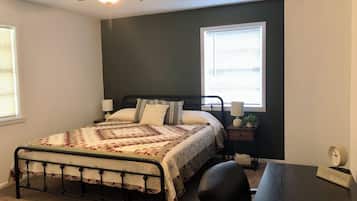 Une chambre à coucher comprenant un lit, deux tables de chevet, un bureau, une chaise, un ventilateur de plafond et deux fenêtres.
