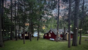 Een chalet met een rode gevel, omgeven door hoge bomen en een gazon.