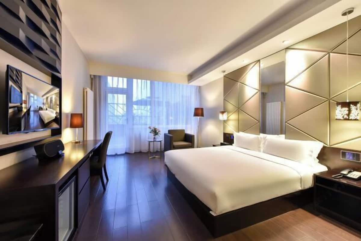 A modern hotel room with a large bed, a desk with a chair, a small table, and a TV.