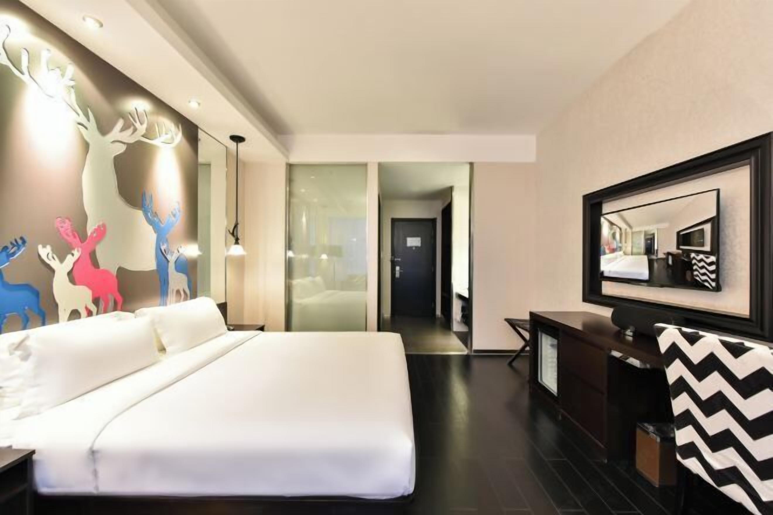 A hotel room with a large bed, a TV, a desk, and a mirror.