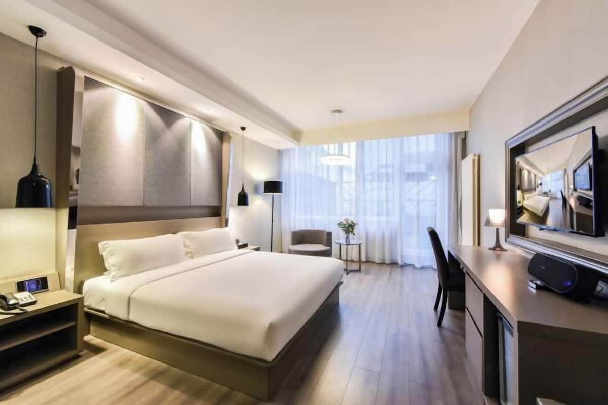 A modern hotel room with a large bed, bedside table with a phone, a desk with a computer, and a large mirror.
