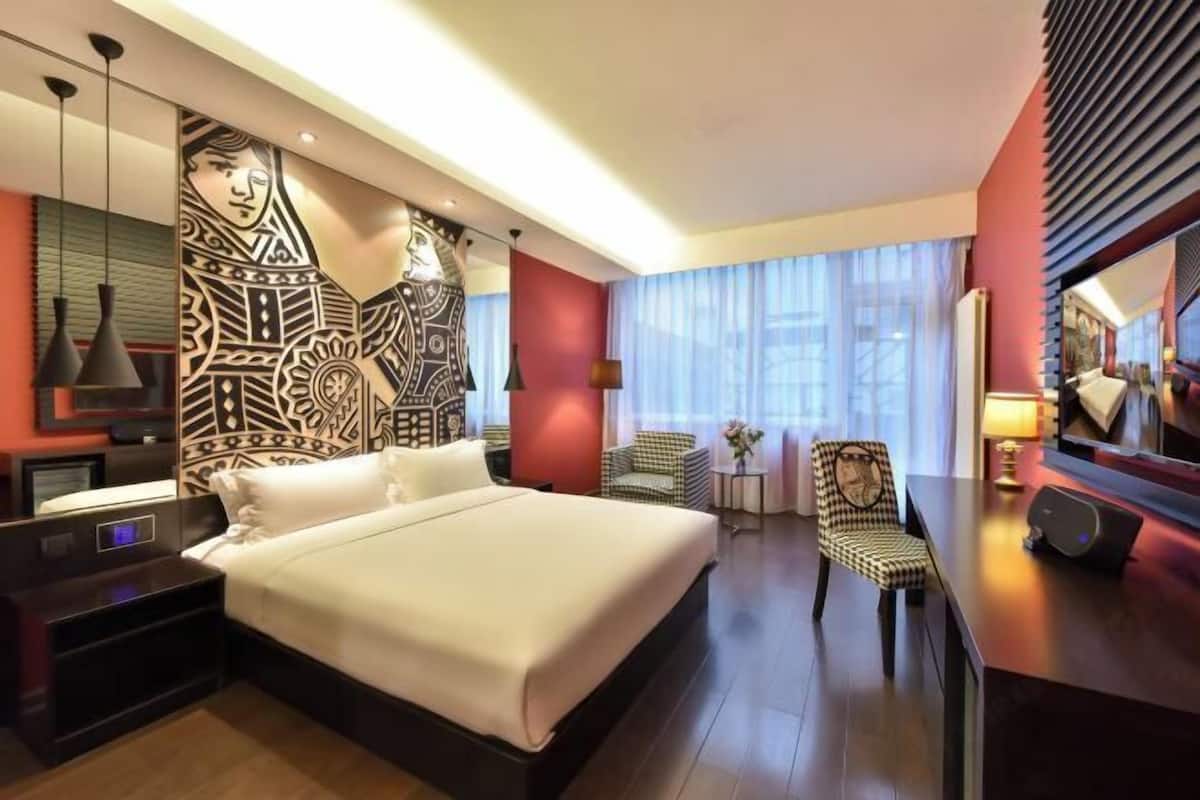 A hotel room with a large bed, a desk, a chair, a TV, and a decorative wall.