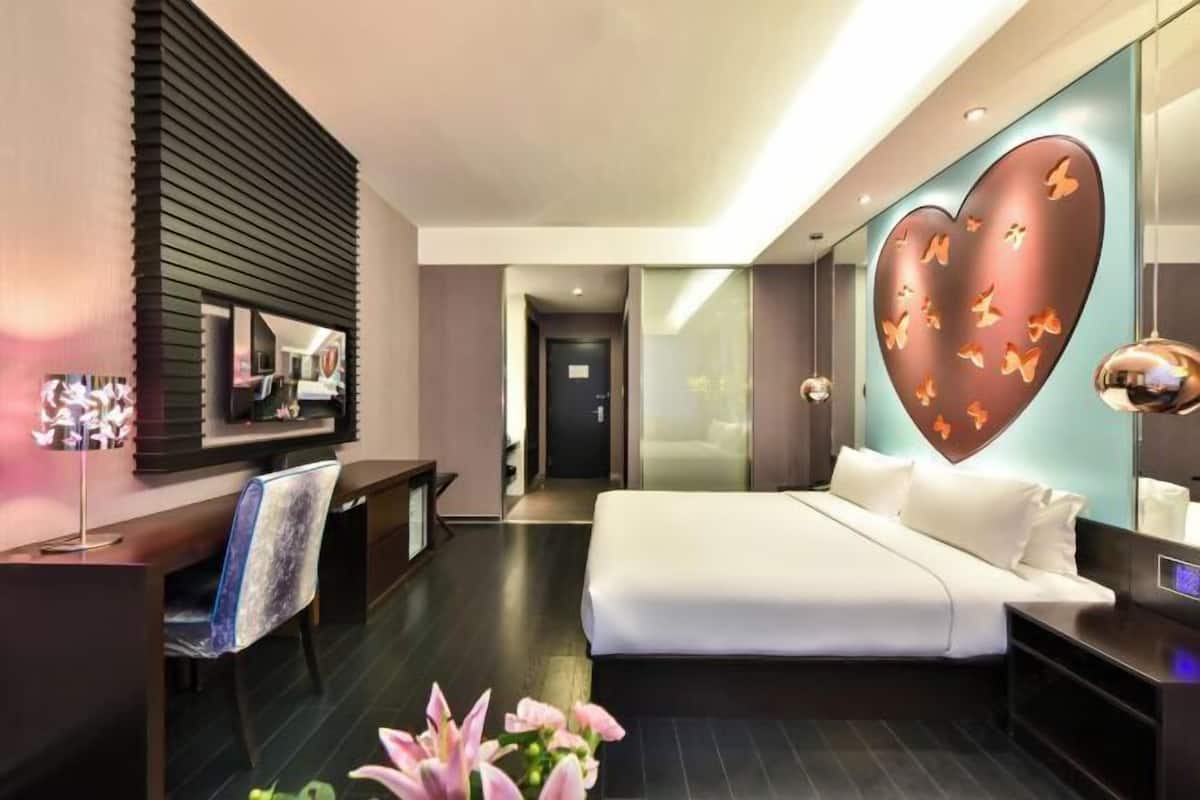 A modern hotel room with a large bed, a desk, a chair, and a mirror.