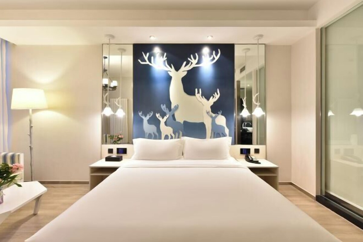 Una habitación de hotel moderna con una cama grande, mesitas de noche, una lámpara y un espejo montado en la pared.