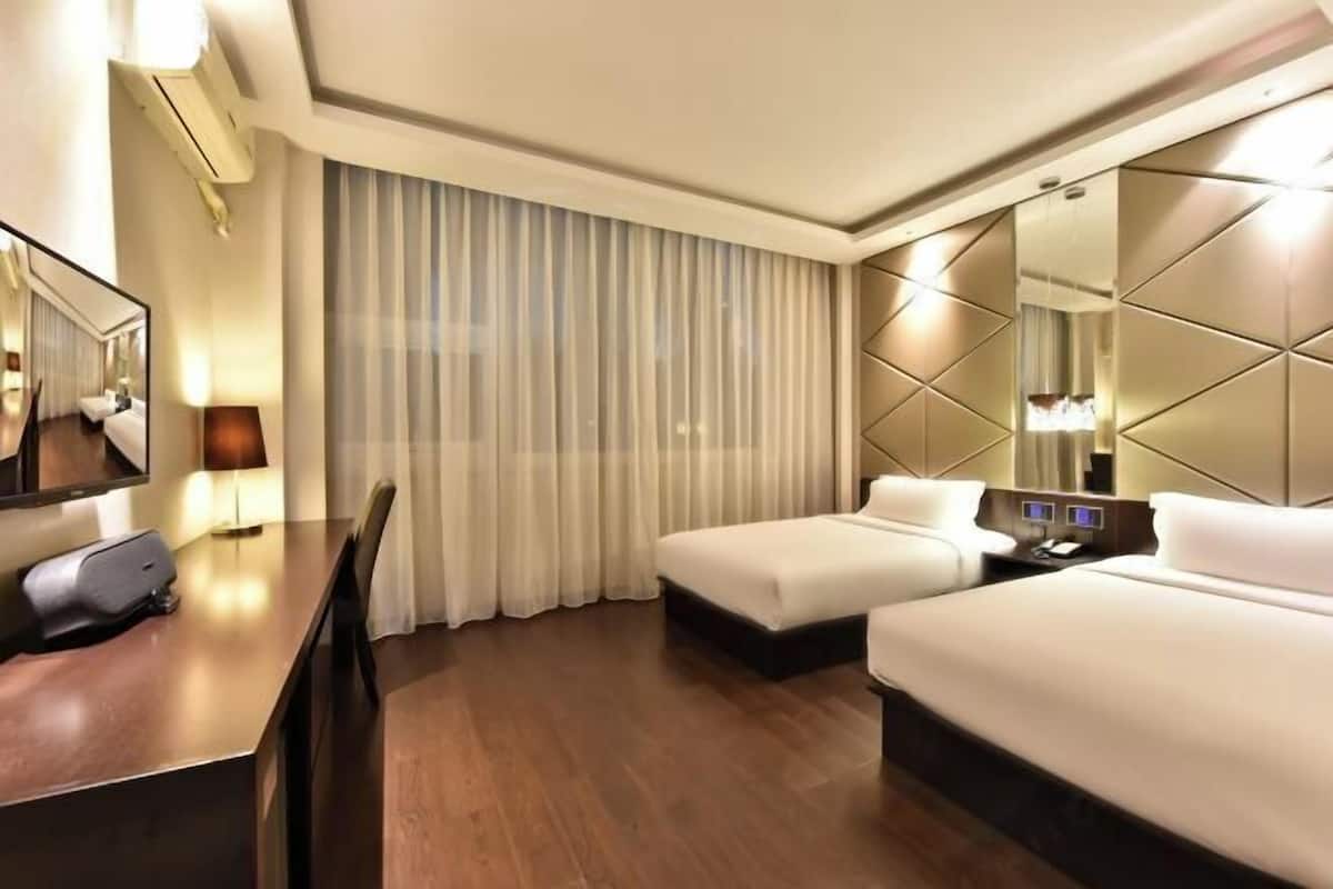 A hotel room with two beds, a desk, a chair, a mirror, and a large window with curtains.