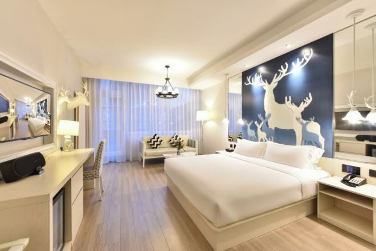 Une chambre d’hôtel moderne dotée d’un grand lit, d’un bureau, d’une chaise, d’un miroir et d’un mur décoré d’œuvres d’art représentant des cerfs.
