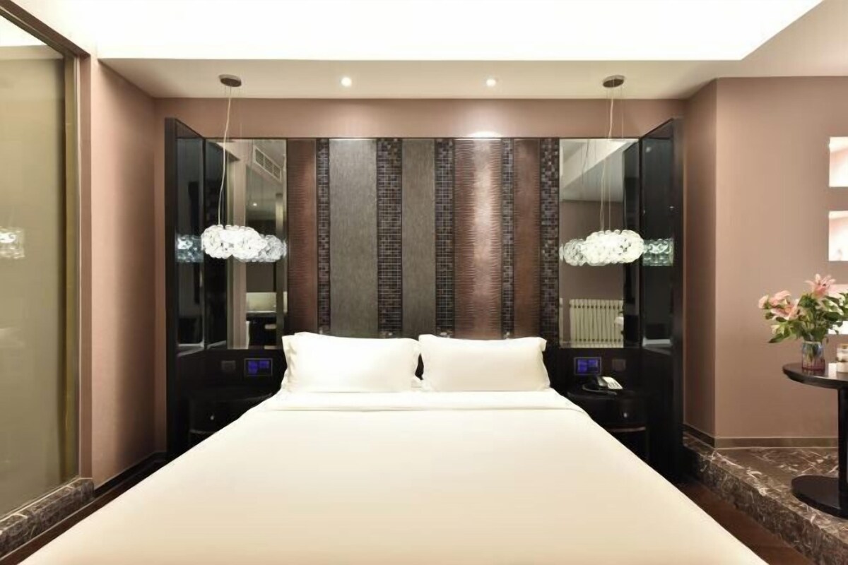 Una habitación de hotel moderna con una cama grande, un espejo y una pequeña mesa con un florero.