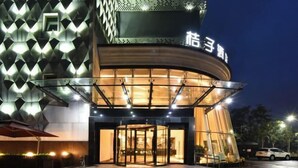 A hotel entrance with a glass revolving door, a modern facade with geometric patterns, and a sign in a foreign language. - Orange Hotel Select (Beijing Yizhuang Wanyuan Street) (Beijing)