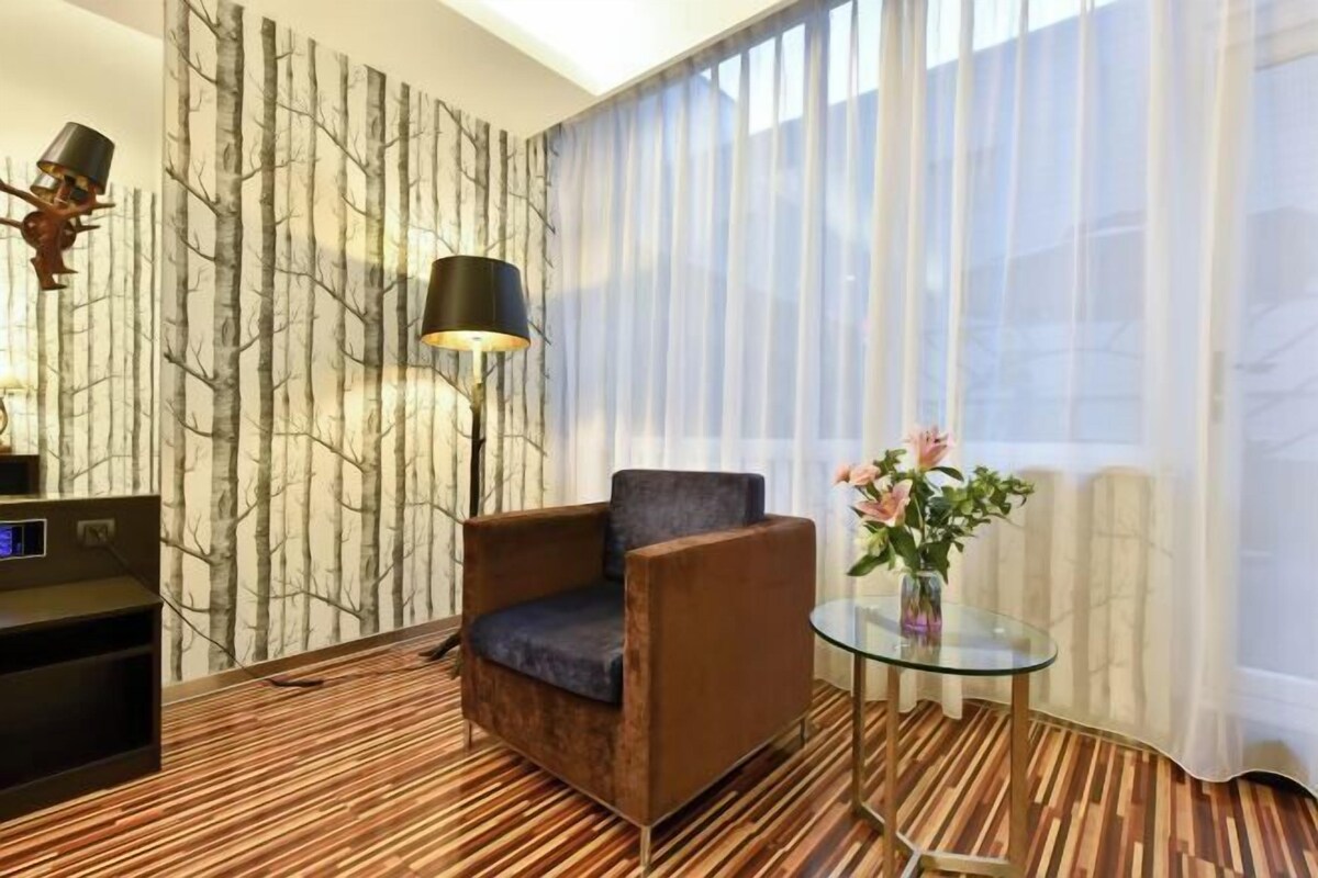Una habitación moderna con papel tapiz estampado, un sillón marrón, una mesa de vidrio con un jarrón y un piso con diseño a rayas.