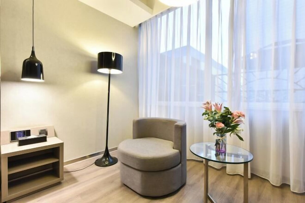 Una habitación moderna con un sofá, una mesa de vidrio con flores, una lámpara de pie y un mueble para la televisión.