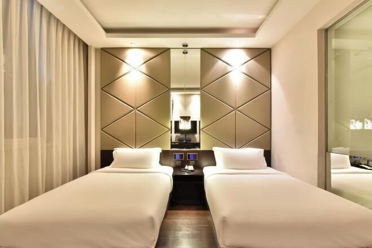 Habitación de hotel con dos camas, un escritorio en el centro y un muro con espejo.