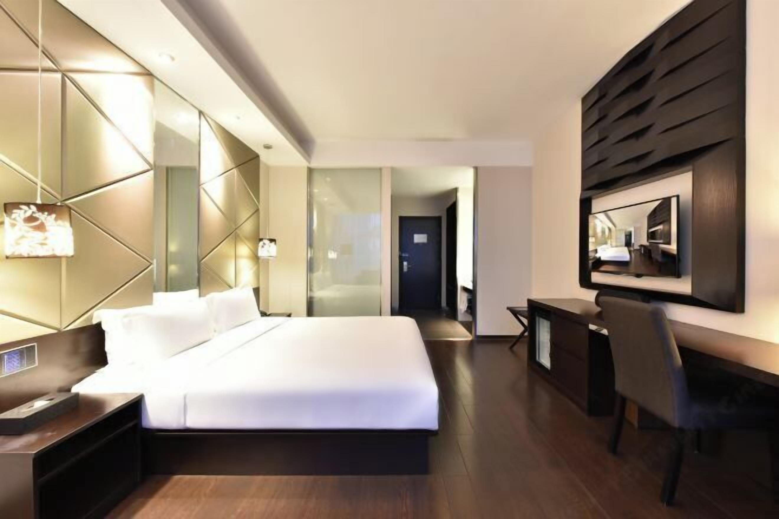 A modern hotel room with a large bed, bedside tables, a desk, and a chair.