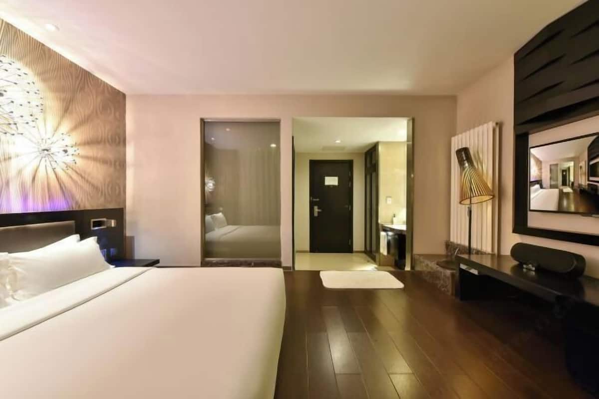 A modern hotel room with a large bed, a desk, a mirror, and a walk-in closet.
