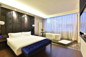 Una habitación de hotel moderna con una cama grande, un banco, una bañera y vistas al exterior.