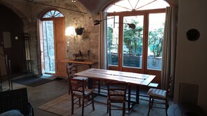 Un comedor rústico con mesa y sillas de madera, paredes de piedra y ventanas grandes con vistas al verdor.