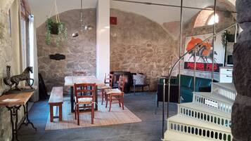 Un interior rústico con paredes de piedra, una mesa de madera con sillas, una chimenea y una escalera con un cartel.