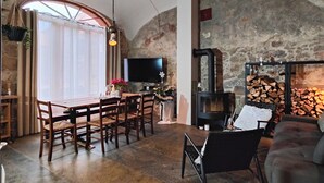 Una sala de estar acogedora con pared de piedra, chimenea, televisor y comedor con mobiliario de madera.