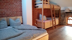 Ein Zimmer mit Etagenbett, Einzelbett und Steinwand.