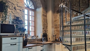 Una cocina con armarios blancos, una pared de piedra, una ventana y una escalera con barandilla de metal.