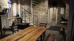 Un interior rústico con una mesa de comedor de madera, paredes de piedra, una escalera y una escultura de caballo.