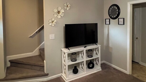 Una sala de estar con un televisor sobre un mueble blanco, una escalera y una puerta.