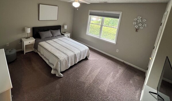 Une chambre à coucher avec un grand lit, une table de chevet, une lampe, une fenêtre et un élément décoratif mural.