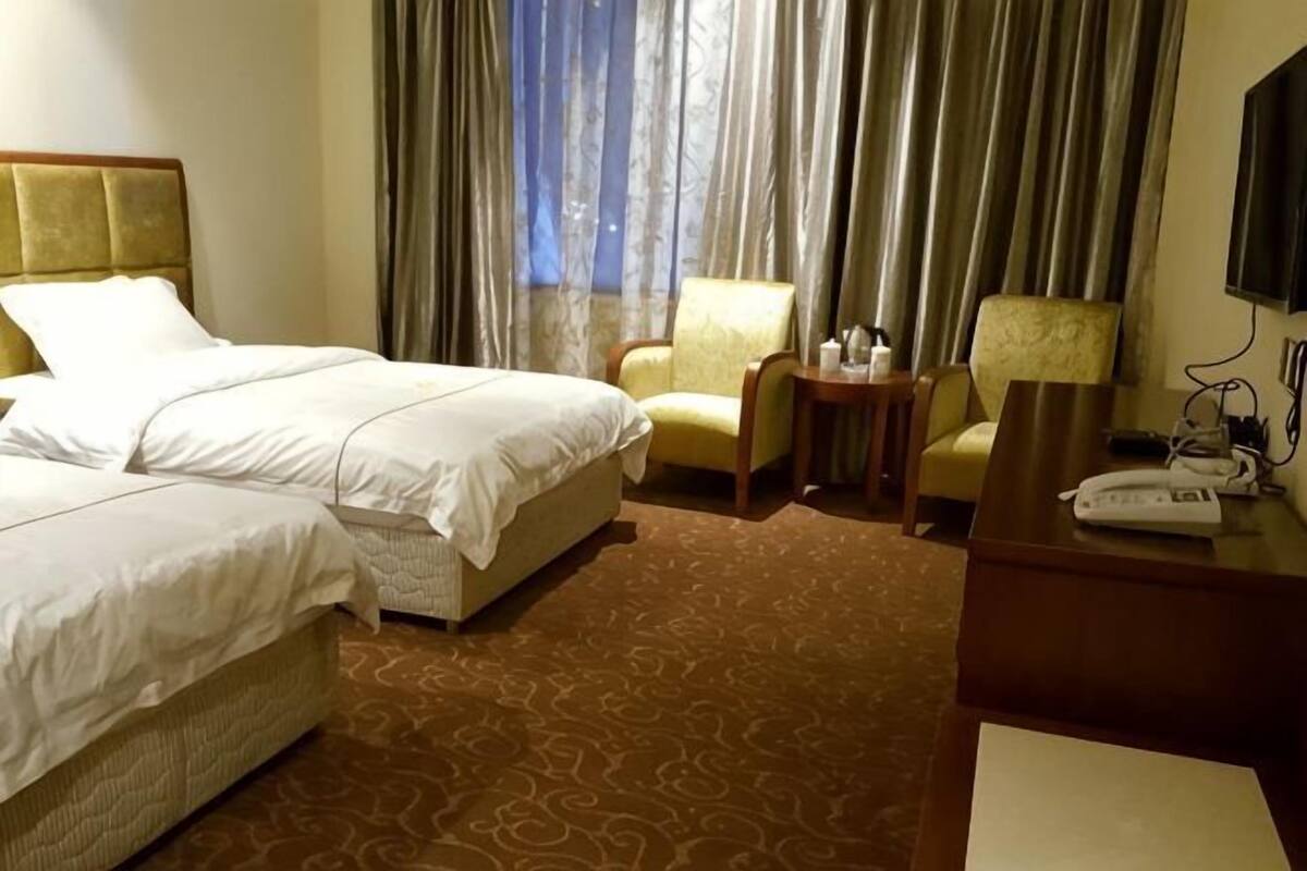 Une chambre d’hôtel avec deux lits, un bureau avec un téléphone, une chaise et un téléviseur.