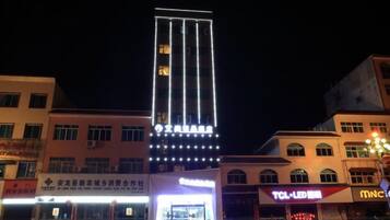 Un edificio de varios pisos con señalización iluminada, una zona comercial en la planta baja con tiendas y un estacionamiento.