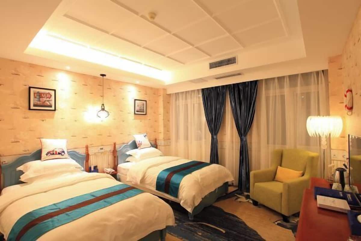 Ein Hotelzimmer mit zwei Betten, einem Schreibtisch, einem Stuhl und einem großen Fenster mit Vorhängen.