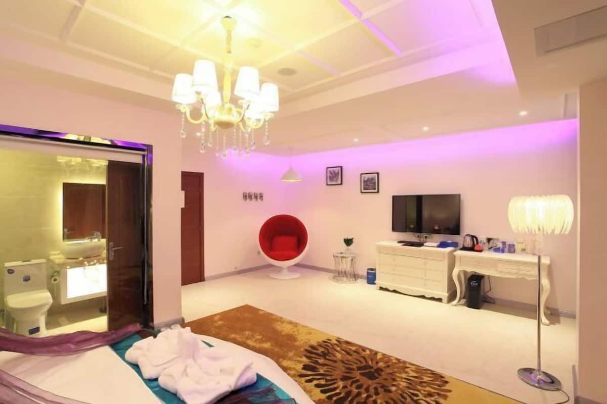 Ein modernes Hotelzimmer mit Bett, einem roten Sessel, einem Fernseher, einem Schreibtisch und einer Chandelier.