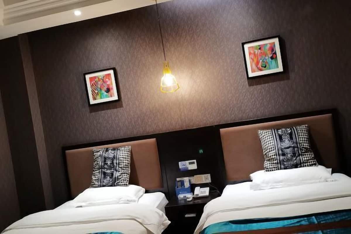 Ein Hotelzimmer mit zwei Betten, einem Nachttisch, einer Wandleuchte und zwei gerahmten Kunstwerken.